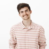 Portrait of good-looking friendly male model with beard and mustache, smiling broadly while talking to coworker, discussing recent news and events in office, standing over gray background. Emotions concept